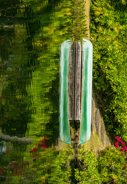 Green canoe on dock reflecting into calm lake or pond in garden by Steve Heap