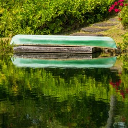 Green canoe on dock reflecting into calm lake or pond in garden