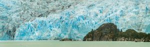 Amalia Glacier rises over large rocks and trees in Patagonia