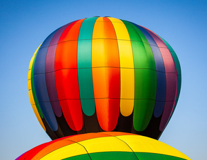 Colorful hot air balloon rising above another with blue sky