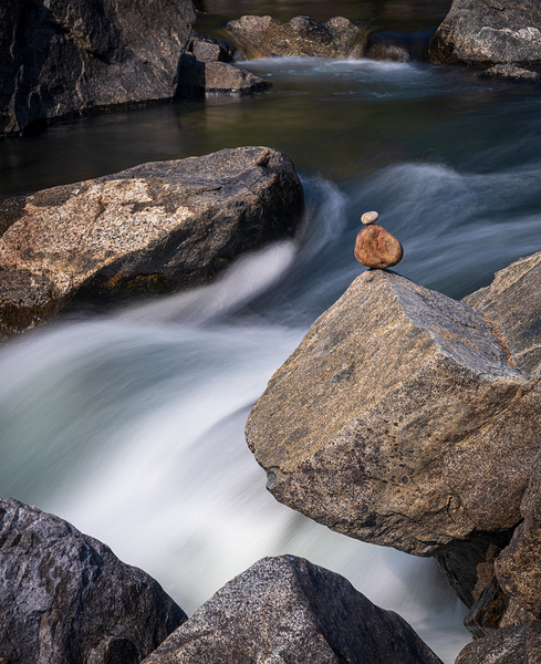 Pebbles balanced on rocks in raging river illustrating resilienc by Steve Heap