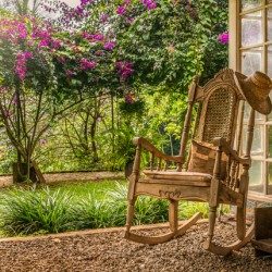 A vintage wooden rocking chair with a straw hat rests on a porch