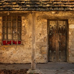 Rustic San Juan building with a barred window red flowers and a