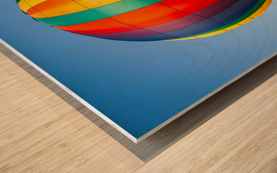 Colorful hot air balloon rising above another with blue sky Wood print